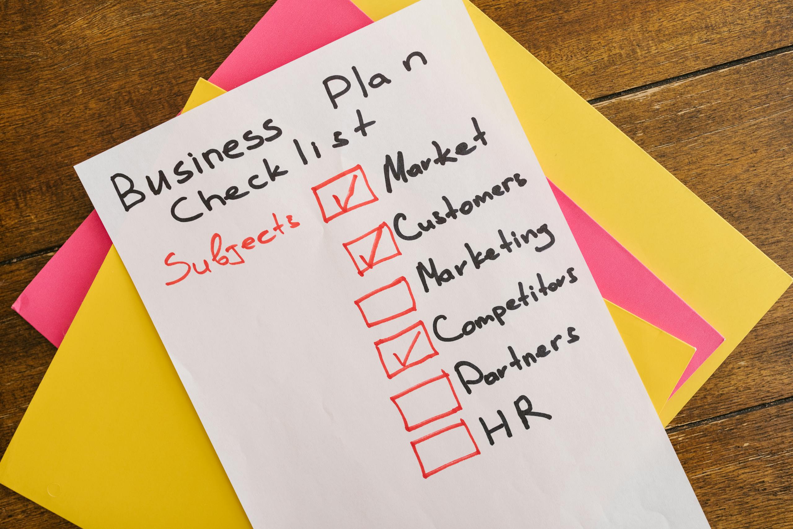 A handwritten business plan checklist on a table with colorful papers indicating important topics for startups.