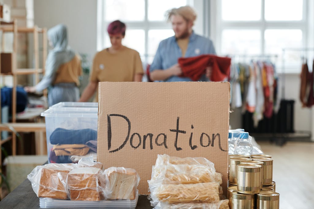 Volunteers sort clothes and food in a donation center. Cardboard sign reads 'Donation.'