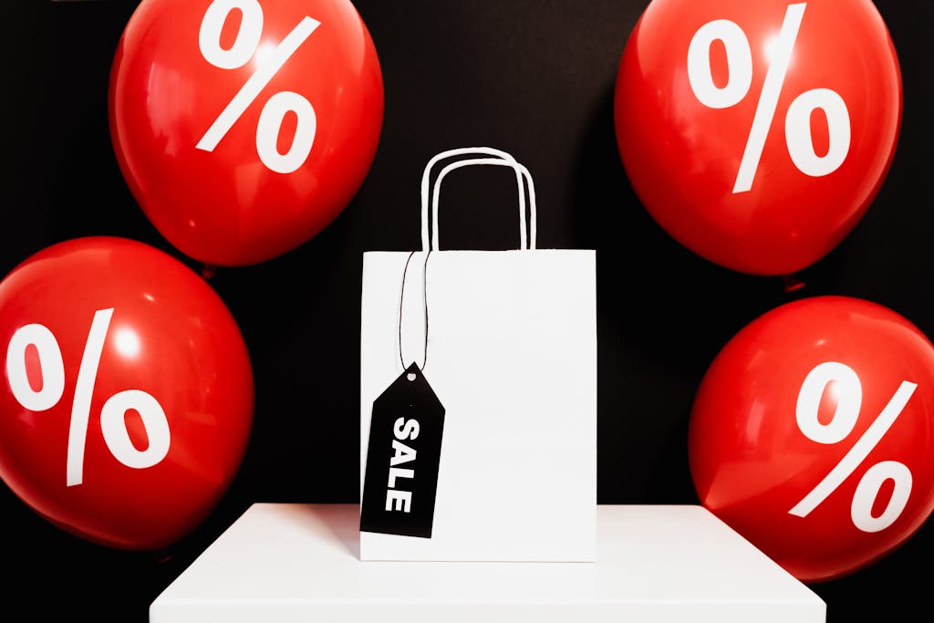 White shopping bag with sale tag surrounded by red balloons displaying percentage signs.